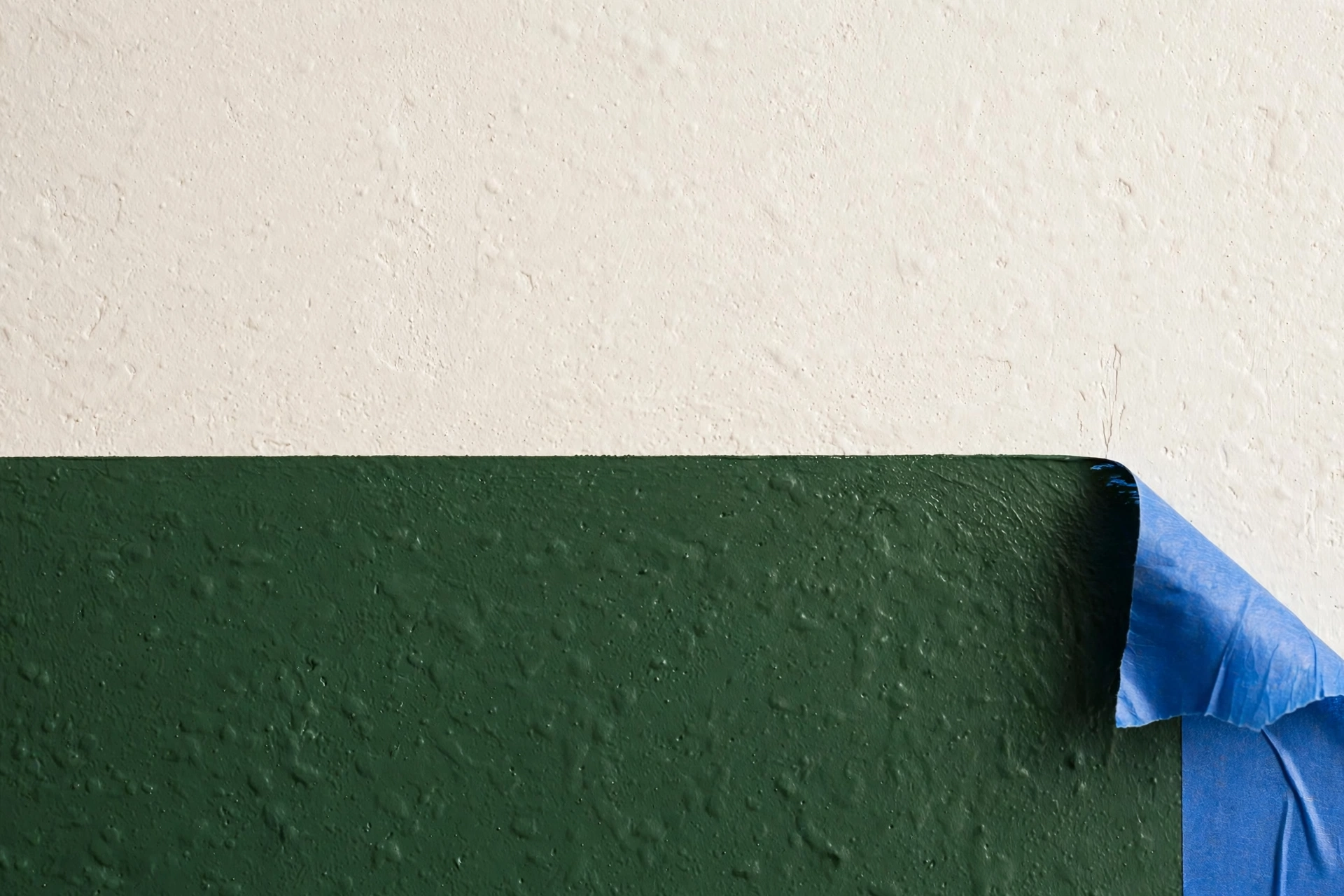 Close-up of a crisp two-tone paint line on a bedroom wall, dark green below and warm white above, with painter's tape edge
